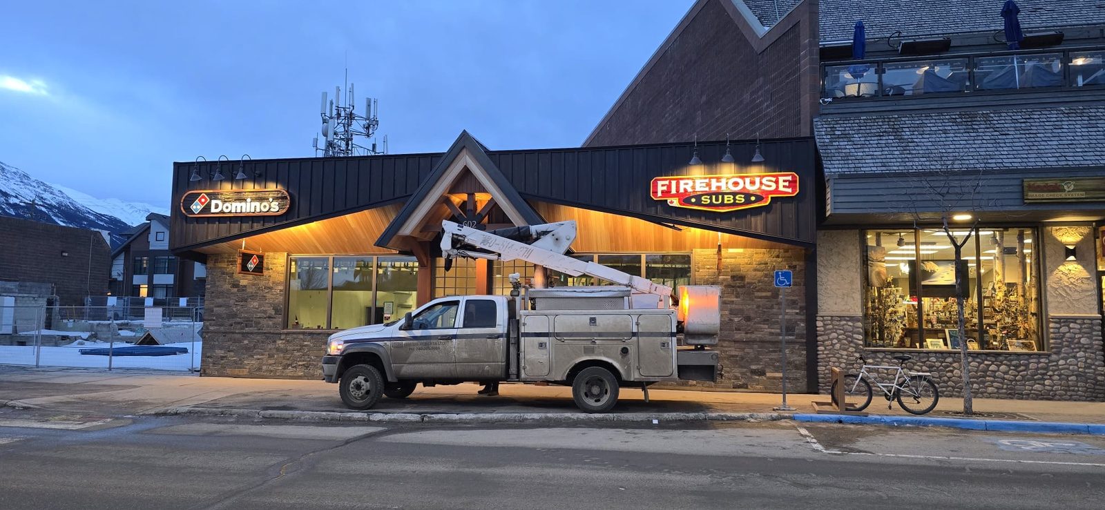 Illuminated Dominos and Firehouse Subs storefront signs at dusk with a Crown Signs service truck