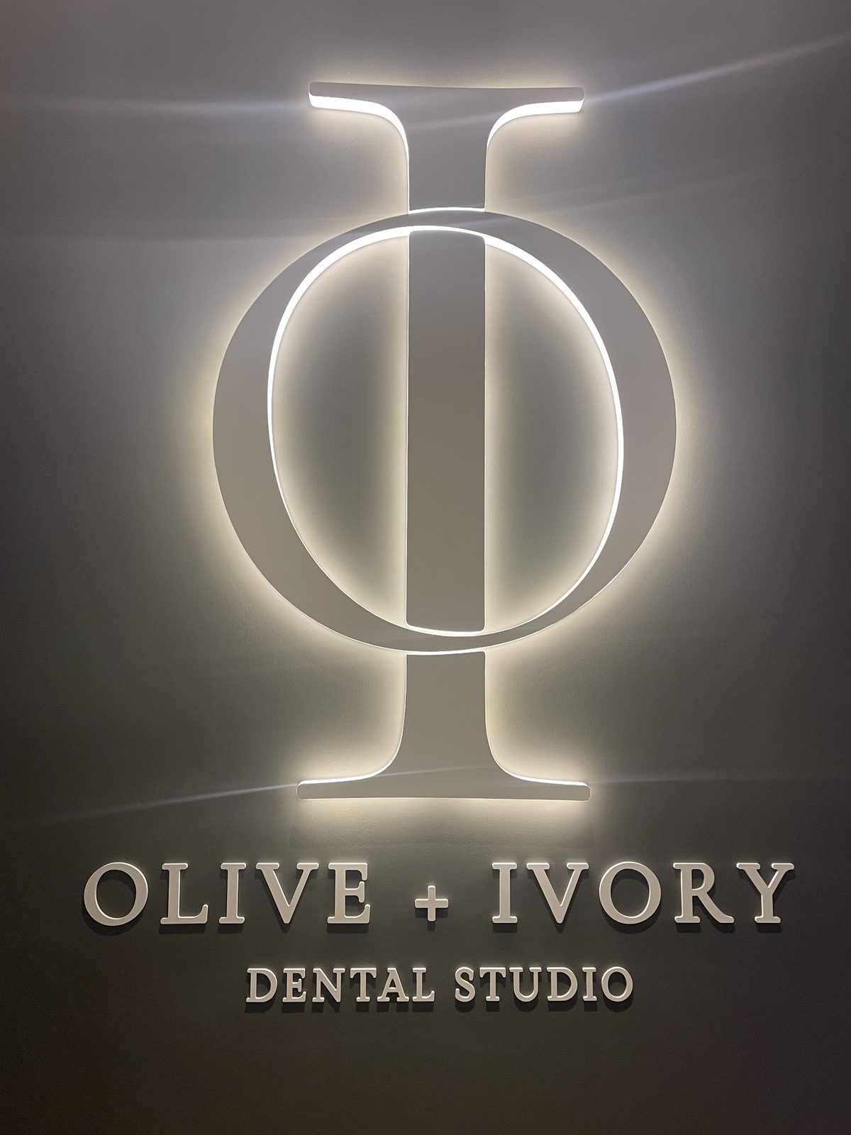 Halo-lit Olive and Ivory Dental Studio interior sign with a backlit monogram